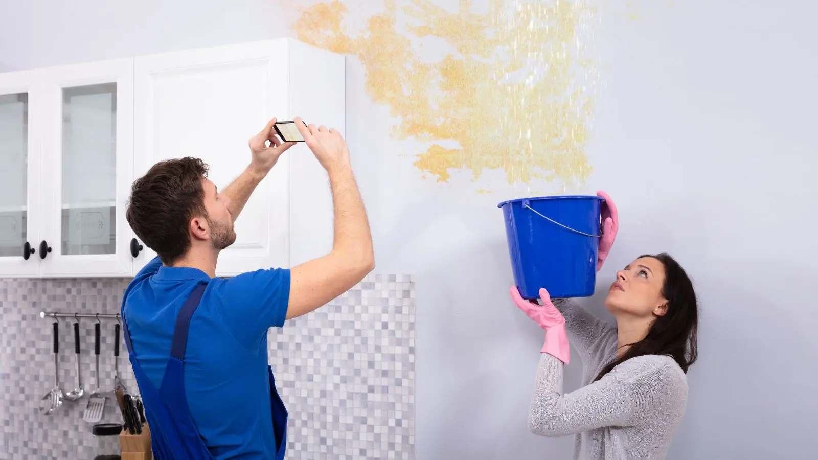 Homeowner photographing a water-stained wall while another holds a bucket