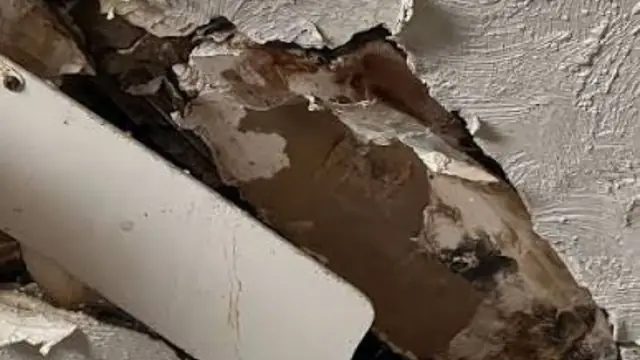 Water-damaged ceiling with crumbling plaster and a visible pipe